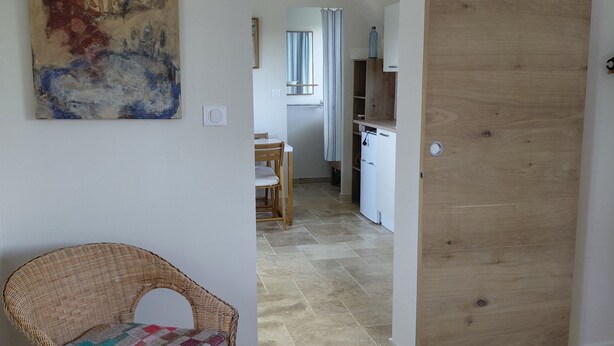 Een kamer met een houten deur, een rieten stoel, een eettafel en een schilderij aan de muur.