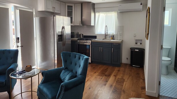 A compact kitchen with modern appliances, a dining area with a blue chair, and a visible bathroom. - Updated Studio in LA with refreshing AC & Washer/Dryer (Los Angeles)