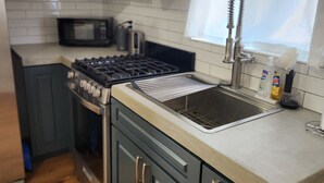 A modern kitchen with grey cabinets, a stainless steel sink, a microwave, and a gas stove. - Updated Studio in LA with refreshing AC & Washer/Dryer (Los Angeles)