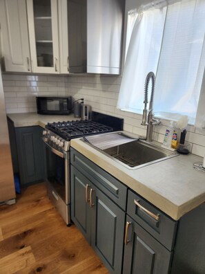 A modern kitchen with grey cabinets, a stainless steel sink, a microwave, and a gas stove. - Updated Studio in LA with refreshing AC & Washer/Dryer (Los Angeles)