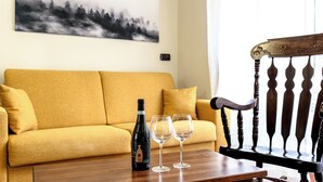 A living room with a yellow sofa, a wooden chair, a table with a wine bottle and two glasses, and a painting on the wall. - La Perla del Sangro (Castel di Sangro)