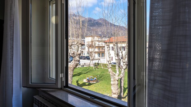 A window with an open view of a playground, buildings, and mountains in the background. - La Perla del Sangro (Castel di Sangro)