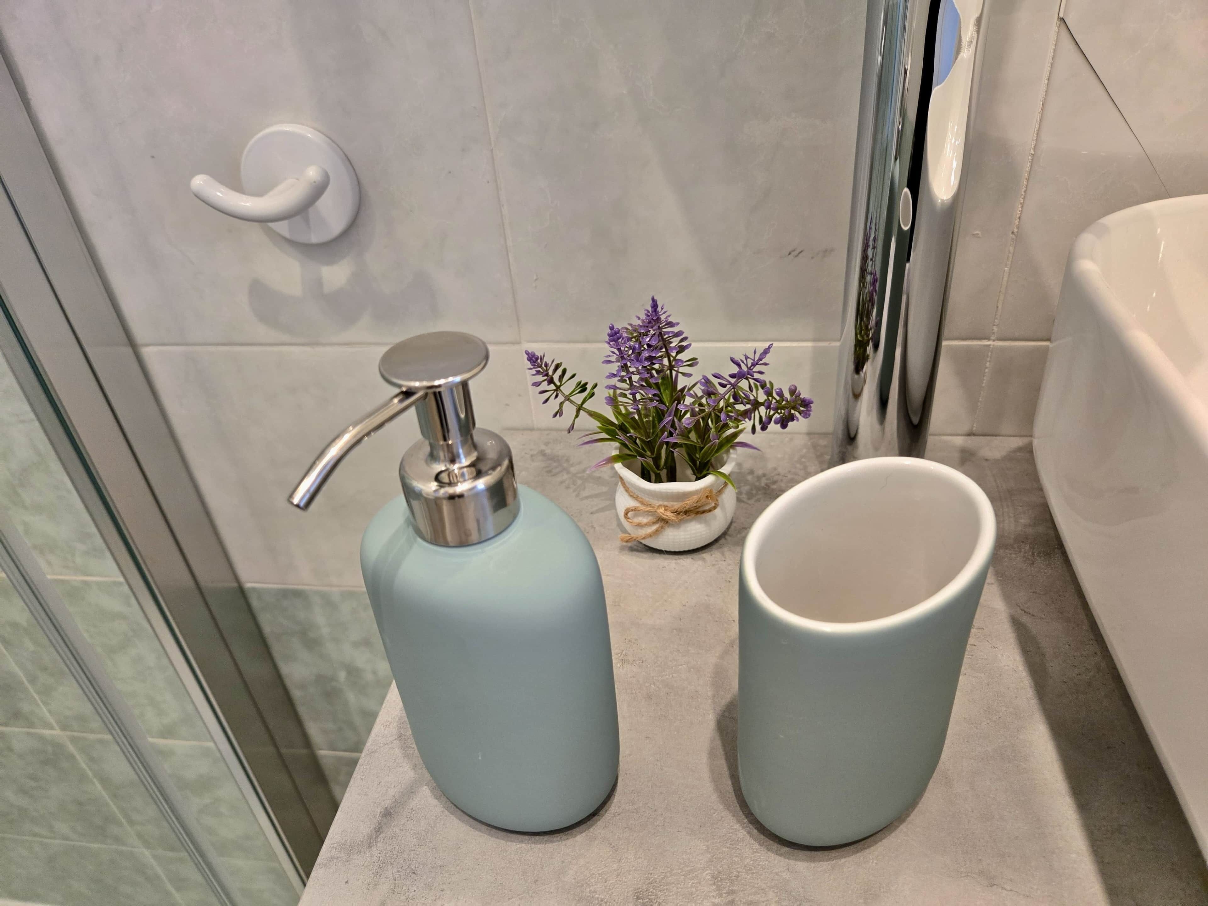 Une salle de bain équipée d’un sèche-mains, d’une petite plante en pot et d’une tasse blanche posée sur le comptoir.