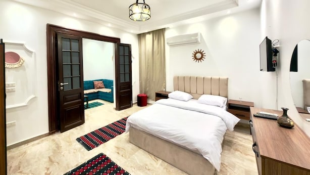 A modern hotel room with a large bed, a desk, and a chair. There is a door leading to another room and a window with curtains. - Spacious 4-bedroom apartment in awesome Giza Governorate with AC (Giza Governorate)