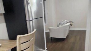 Una cocina compacta con un refrigerador moderno, una mesa de comedor con sillas, y un sillón blanco en la habitación contigua.