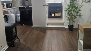 Un espacio habitable compacto con lavadora y secadora, una pequeña cocina, un tocador azul oscuro y una planta en maceta.