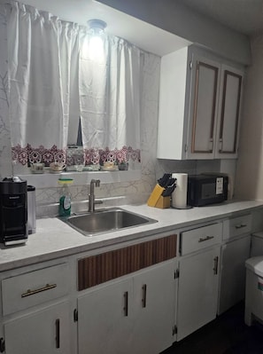Una cocina con un fregadero, cafetera, microondas y armarios.
