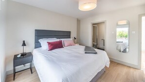 A modern bedroom with a large bed, a nightstand, a mirror, and a ceiling light.