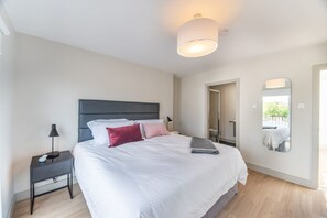 A modern bedroom with a large bed, a nightstand, a mirror, and a ceiling light. - Elegant 1BR Stay in the Heart of Dublin (Dublin)