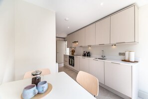 A modern kitchen with white cabinets, a white countertop, and a dining area with a table and chairs.
