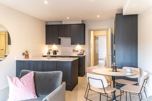 A modern kitchen with dark cabinets, a central island, and a dining area with a round table and chairs.
