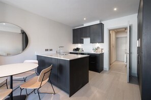 A modern kitchen with a central island, dark cabinetry, and a dining area with a round table and chairs. - Comfortable 1BR Residence on Montague Street (Dublin)