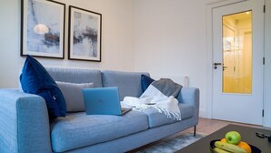 A modern living room with a grey sofa, a laptop, and a bowl of fruit on a coffee table. - Elegant City 1BR at St Stephen's Green (Dublin)