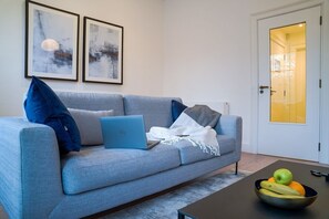 En moderne stue med en grå sofa, en bærbar computer og en skål med frugt på et sofabord.