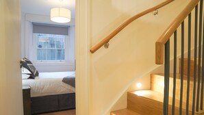 Een trap met houten treden en zwarte leuningen die naar een slaapkamer leidt, met een bed en een raam.