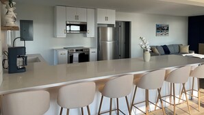 Una cocina moderna con armarios blancos, electrodomésticos de acero inoxidable y una isla central con taburetes de bar.