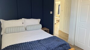 Un dormitorio con cama, almohadas, una mesita de noche y una puerta.