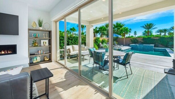 A modern living room with a fireplace, a glass-enclosed patio with outdoor furniture, and a pool. - Platinum Luxury @ PGA West (La Quinta)