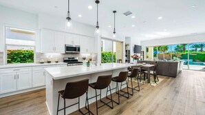A modern kitchen with a large island, white cabinetry, and a dining area with bar stools. - Platinum Luxury @ PGA West (La Quinta)