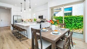 A modern kitchen with white cabinets, a central island, and a dining area with a table set for four. - Platinum Luxury @ PGA West (La Quinta)
