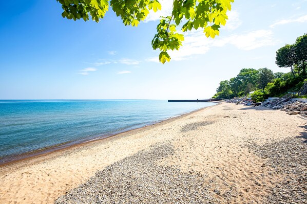 A beach with clear water and pebbles, surrounded by trees.