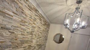 A room with a stone-patterned wall, a yellow sofa with a brown blanket, a wooden floor, and a white door. - Superb Moorehouse Holiday Let private garden games room  & bar Pet freindly! (Thornton-Cleveleys)