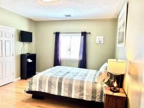 Une chambre à coucher avec un lit, une télévision, une fenêtre avec des rideaux, une lampe de chevet et une porte.