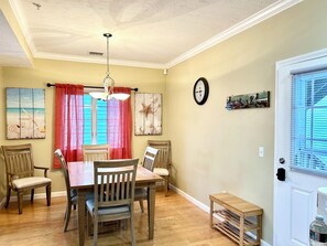 Une salle à manger avec une table et des chaises en bois, un ventilateur de plafond et une horloge au mur.