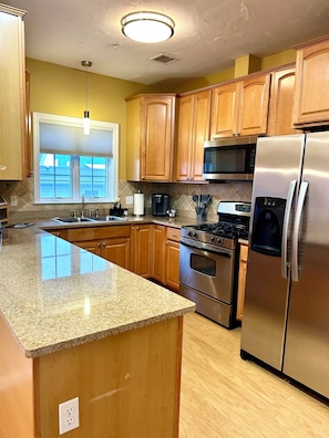 A kitchen with wooden cabinets, stainless steel appliances, granite countertops, and a window with blinds. - Spacious 2-bedroom, 2 bathroom, 2 car parking just steps to beach. (Hampton)