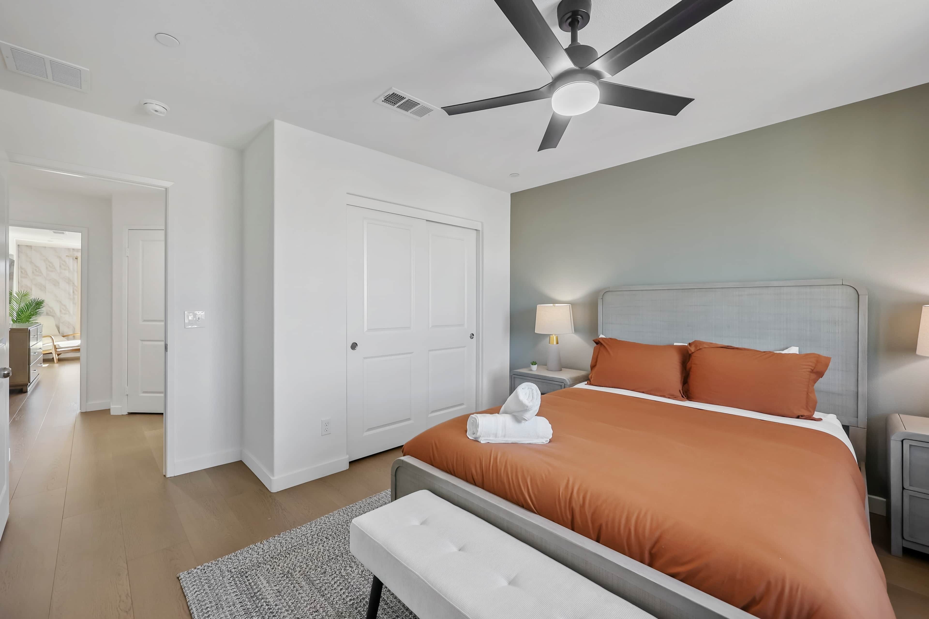 A hotel room with a bed, a ceiling fan, a nightstand, and a door leading to another room.