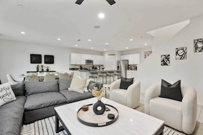 A modern living room with a grey sectional sofa, a white coffee table, and a kitchen in the background. - Resort Game Room Heated SwimUpBar Geyser Mini Golf (Coachella)