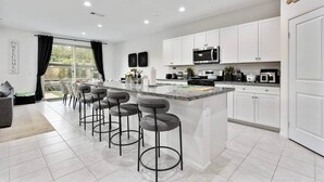 Una cocina moderna con armarios blancos, una isla central con taburetes y un horno microondas y cocina.
