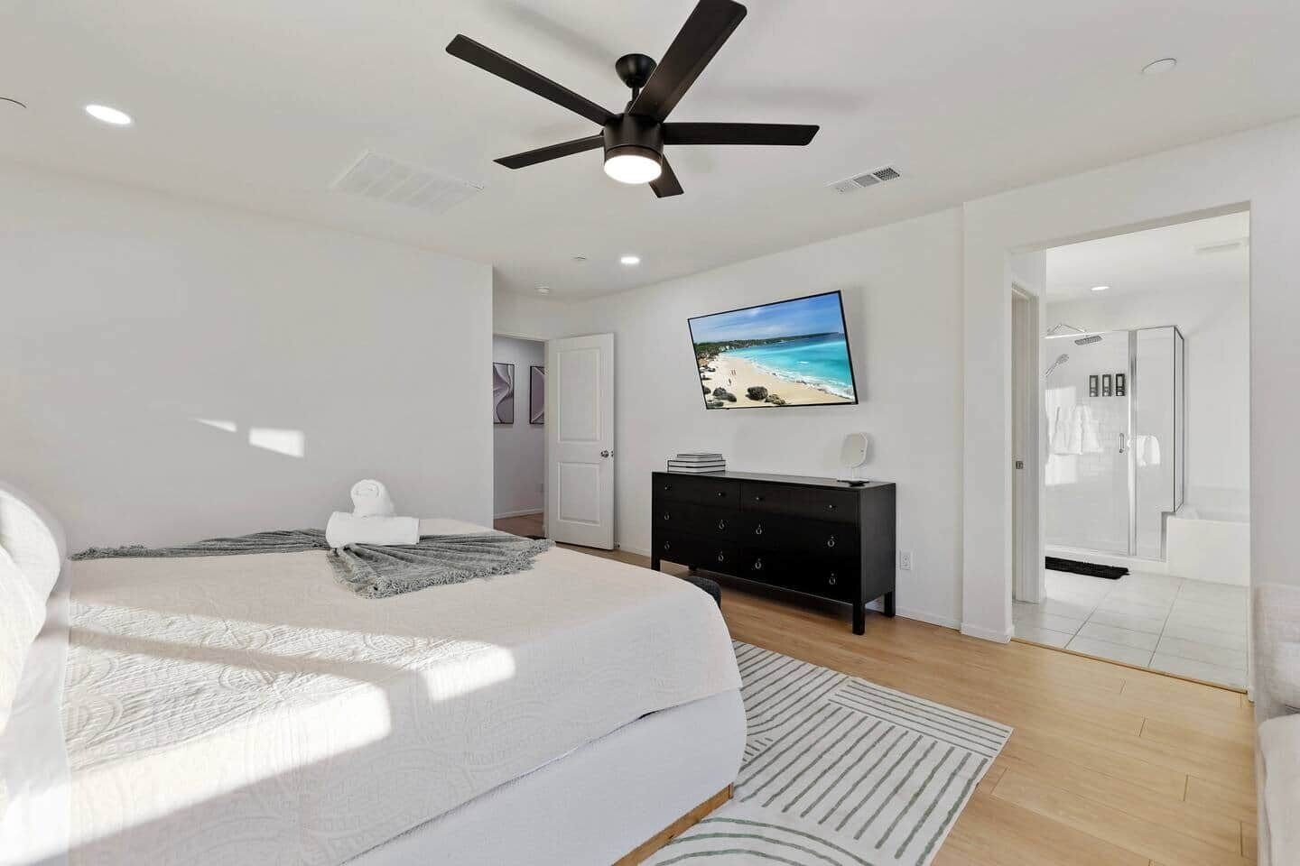A modern bedroom with a bed, a ceiling fan, a TV, and a walk-in closet.