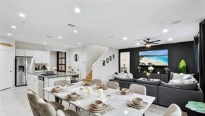 Una cocina moderna con armarios blancos, horno empotrado y comedor con una mesa blanca dispuesta para seis comensales.