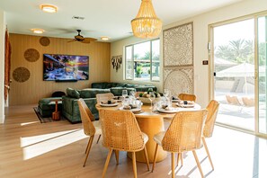 Ein modernes Wohnzimmer mit einem grünen Sofa, einem Esstisch für sechs Personen und einem großen Flachbildfernseher an der Wand.