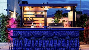 Cocina exterior con barra, incluyendo taburetes y un letrero que indica que es una cocina al aire libre.
