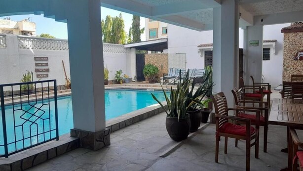 A covered outdoor area with a swimming pool, seating, and potted plants. - Global African Apart-Hotel Mtwapa (Mtwapa)