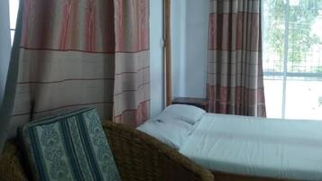 Una habitación con cama, una silla y ventana con cortinas.