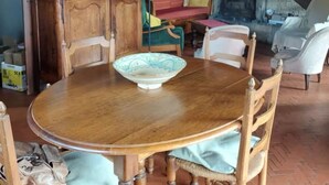 Een gezellige woonkamer met een houten eettafel, stoelen, een boekenkast, een open haard en een trap.