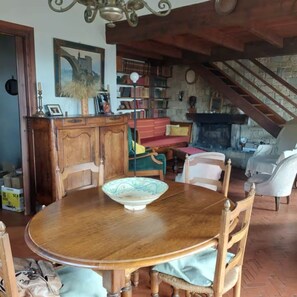 A cozy living room with a wooden dining table, chairs, a bookshelf, a fireplace, and a staircase. - Beautiful family home with sea view (Carqueiranne)