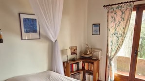 Een slaapkamer met een groot bed, houten plafond, een boekenkast en een raam met gordijn.