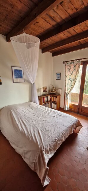 A bedroom with a large bed, a wooden ceiling, a bookshelf, and a window with a curtain. - Beautiful family home with sea view (Carqueiranne)