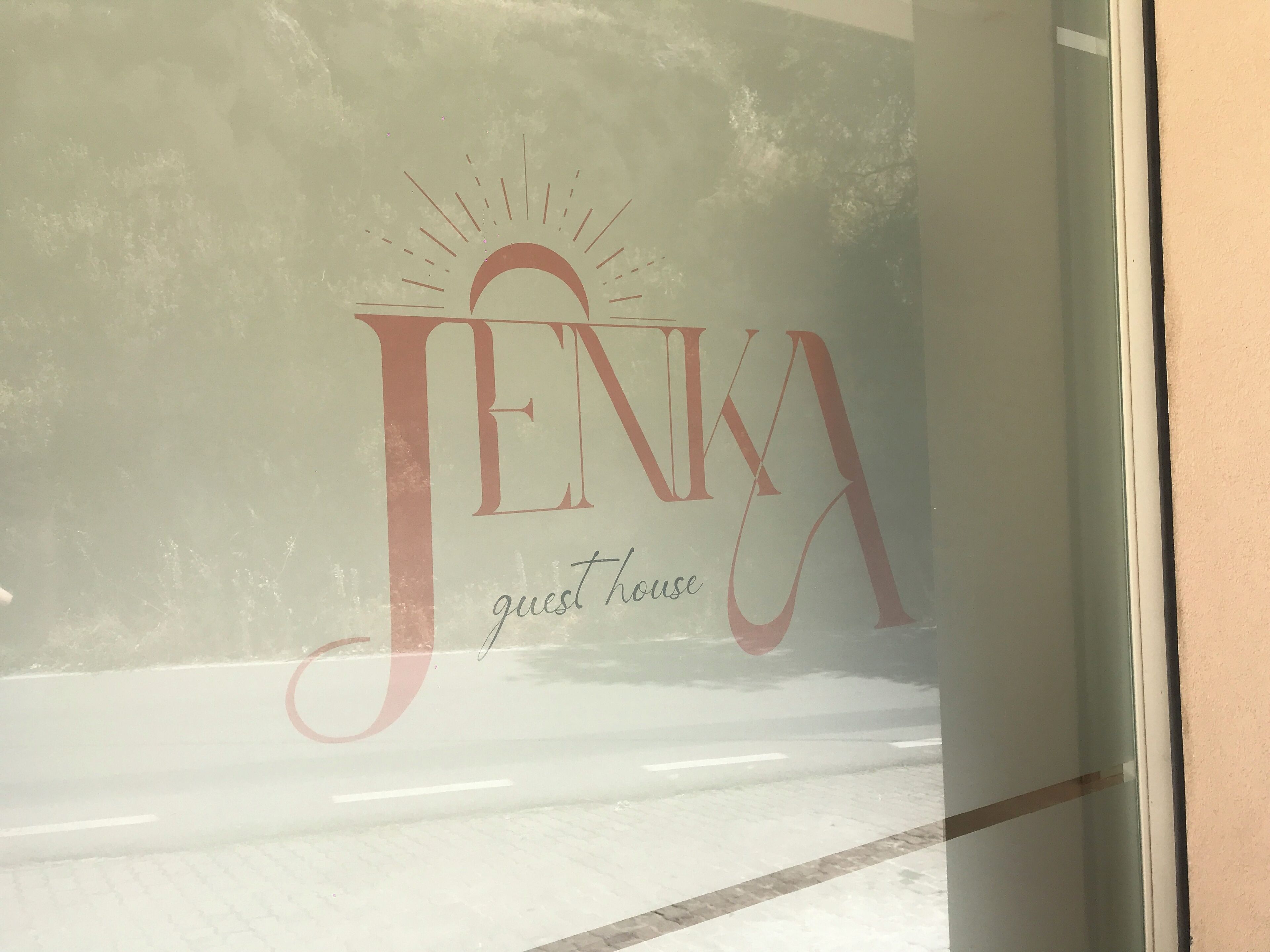 Una finestra de vidre amb la inscripció "JENKA guest house" i un dibuix de sol a la part superior.