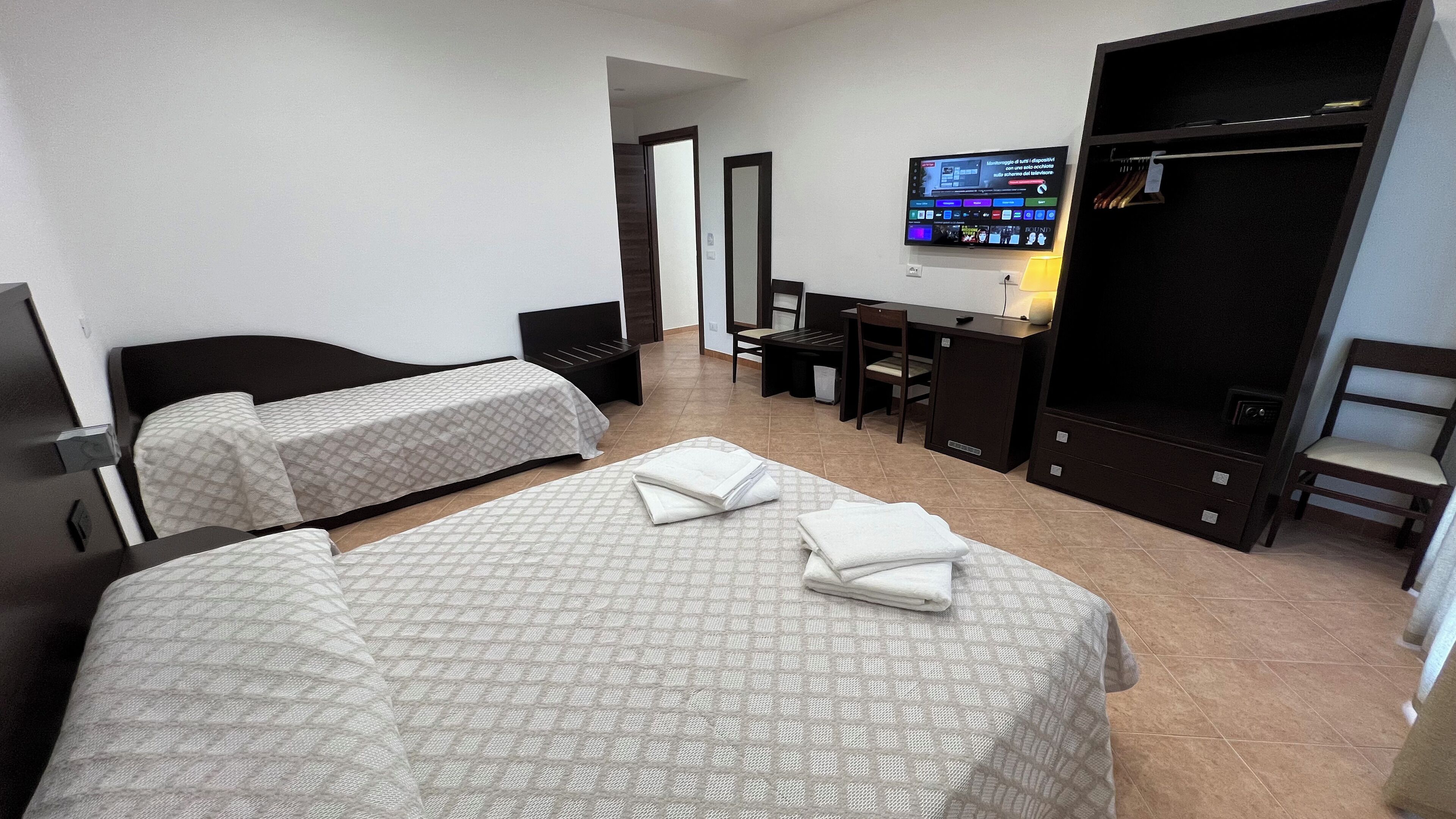 A hotel room with two beds, a desk, a chair, a TV, and a wardrobe.