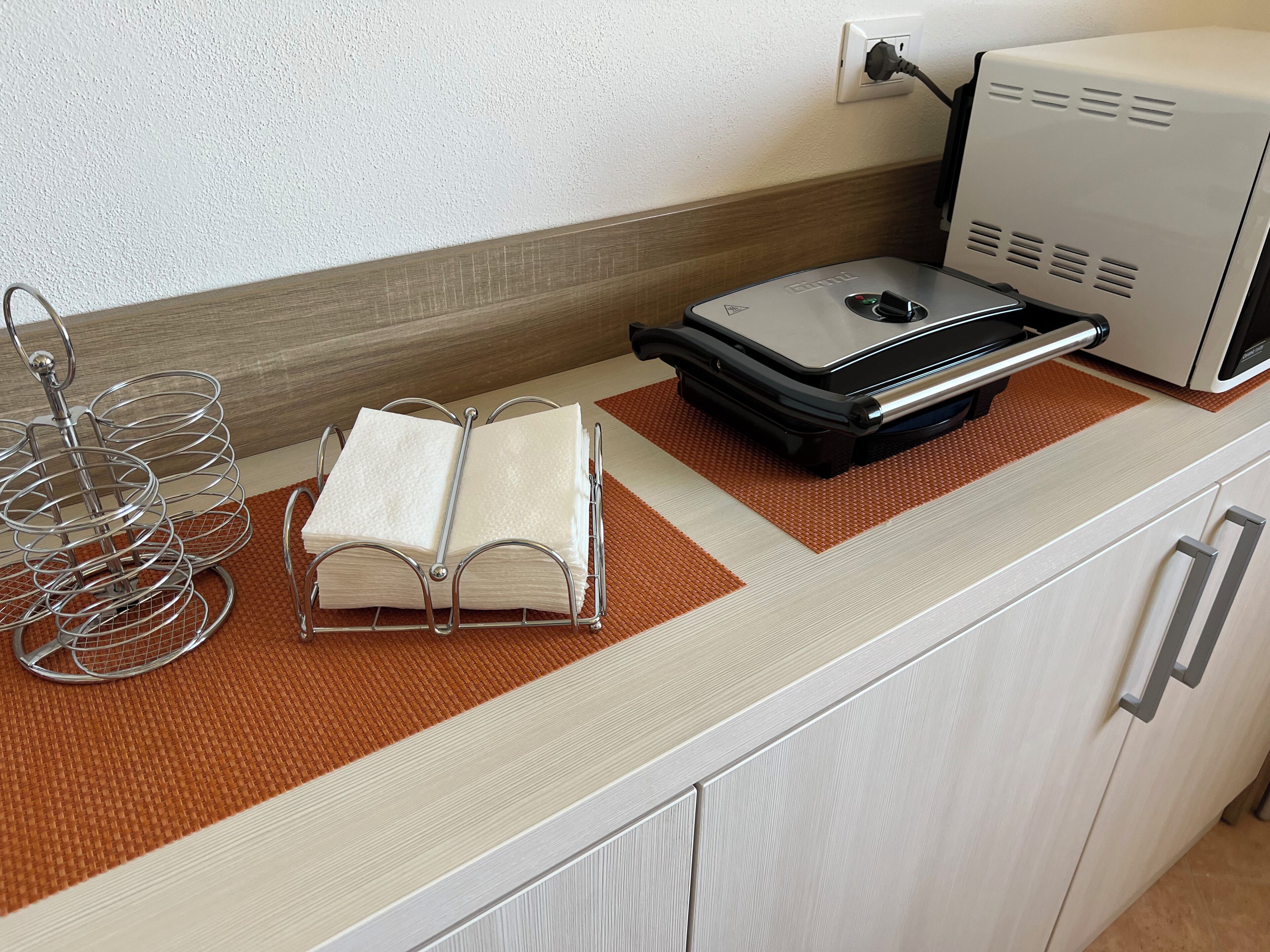 Una encimera de cocina con un microondas, un hervidor y una rejilla metálica con libros.