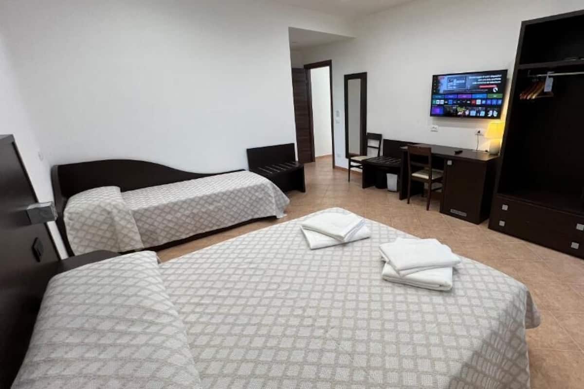 A hotel room with two beds, a desk, a TV, and a wardrobe.