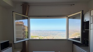 Eine kleine Küche mit Esstisch und Stühlen, ein Fenster mit Blick auf eine entfernte Landschaft und ein eingebauter Mikrowellenherd.