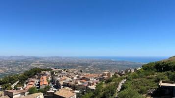 Une ville aux bâtiments aux toits de tuiles rouges, avec une route sinueuse et une vue sur la mer au loin.