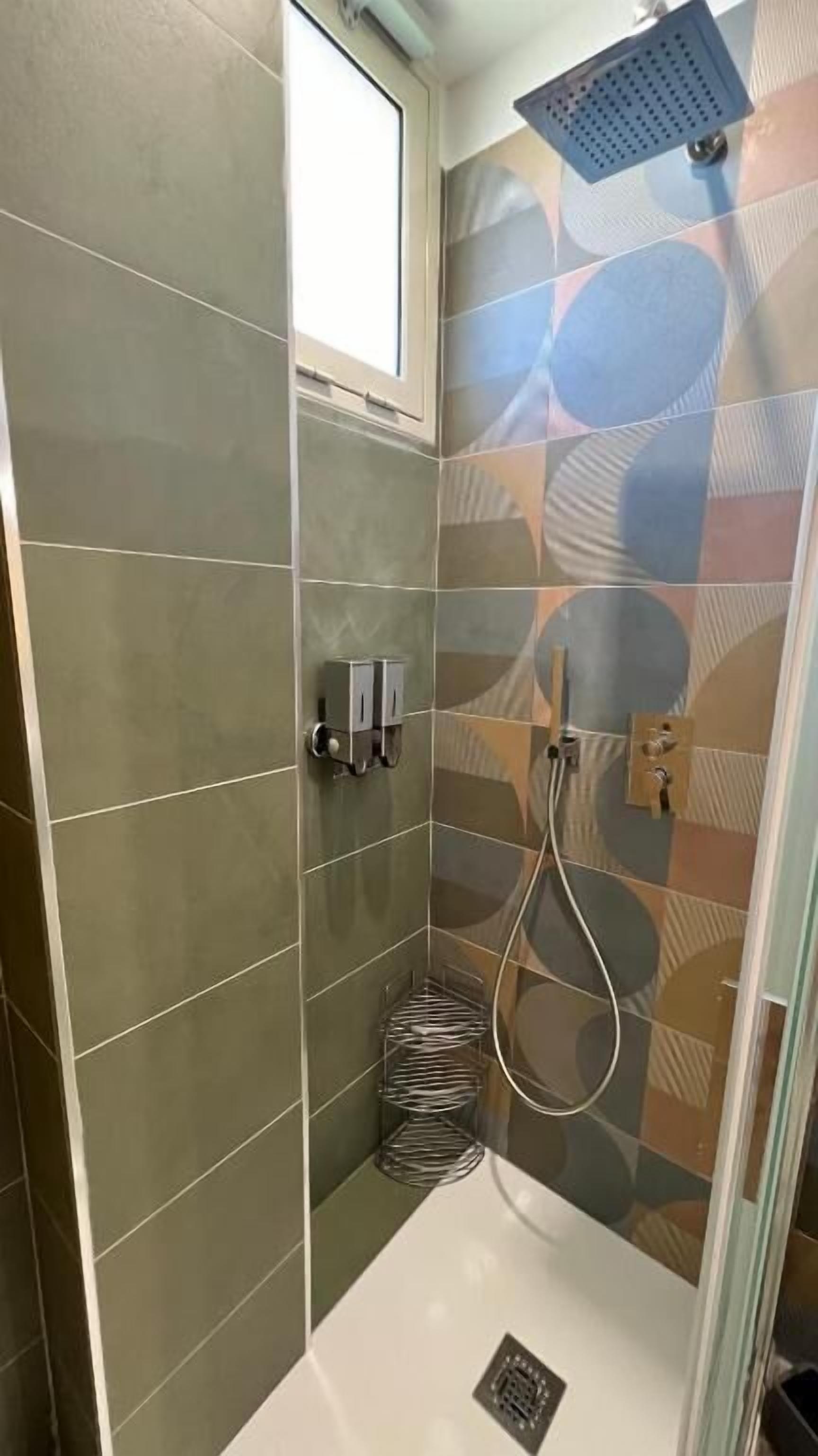 Una ducha con puerta de vidrio, paredes de azulejos y ducha de lluvia.