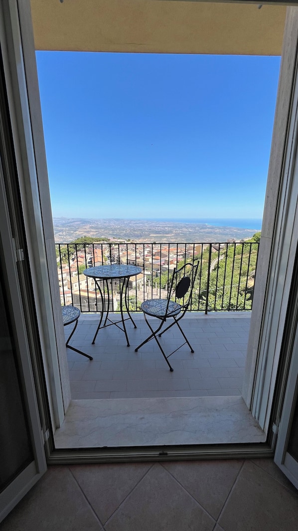 A balcony with a table and chairs, offering a view of a distant landscape. - Jenka (Caltabellotta)